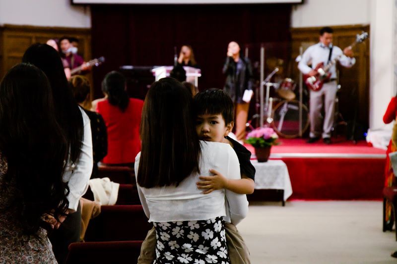 boy in mother's arms looking over her shoulder at church